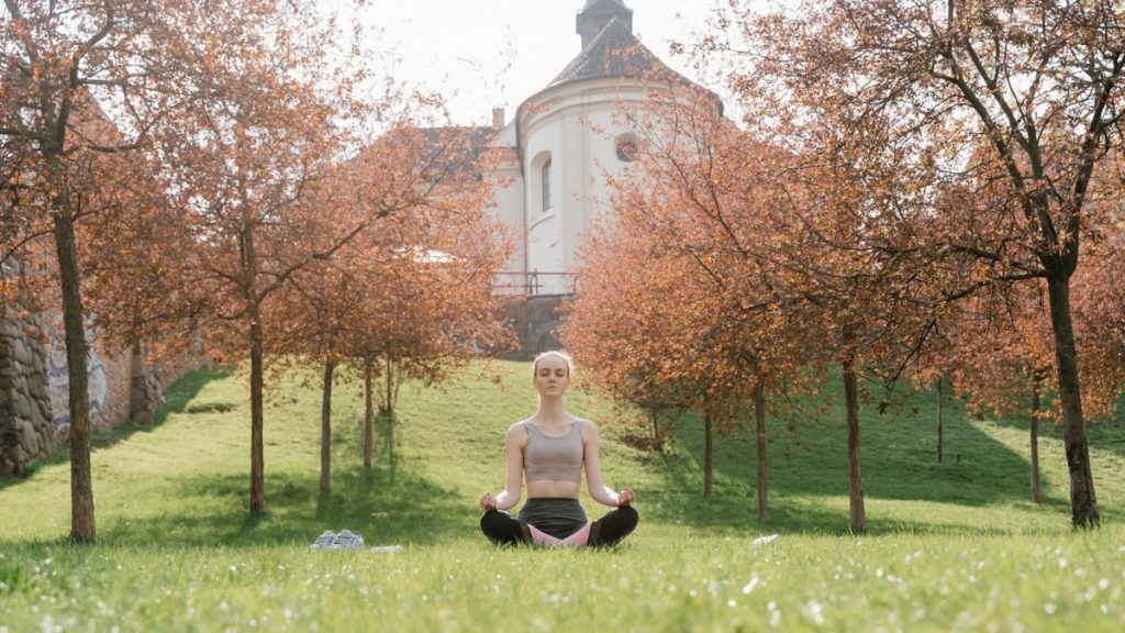 A woman practices meditation outdoors in a tranquil park during fall.